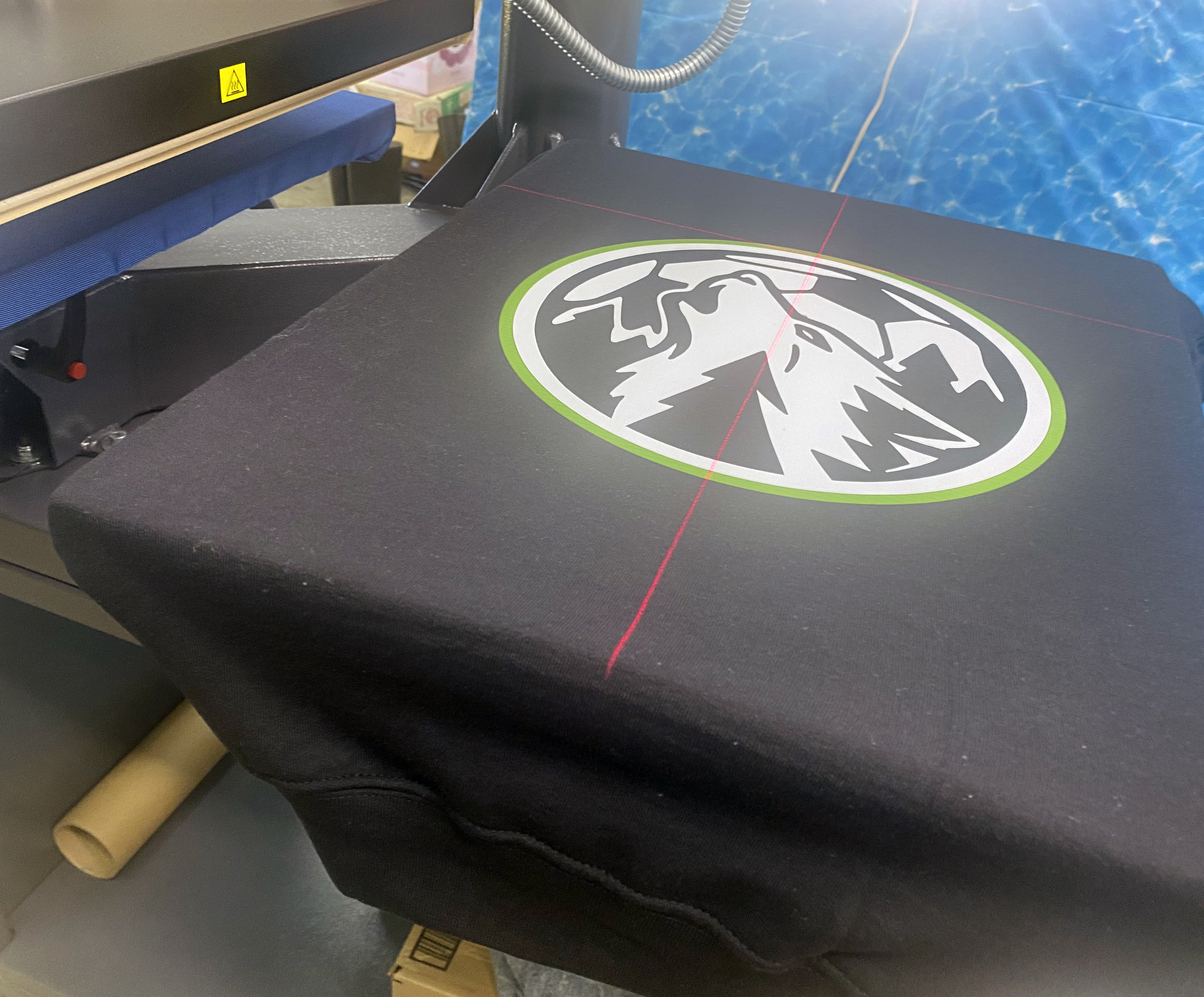 Custom logo being lined up on a hoodie on the heat press at Sport X Canada.